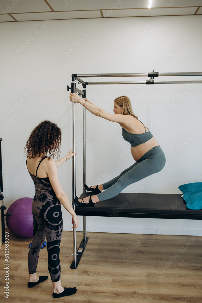 pregnant woman pilates reformer roll up cadillac exercise with personal  trainer Photos | Adobe Stock