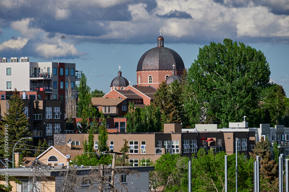 Obraz premium Incredible red brick temple with large metal dome with rust modern white buildings large round leafy trees apartments and offices sports courts blue skies with white clouds