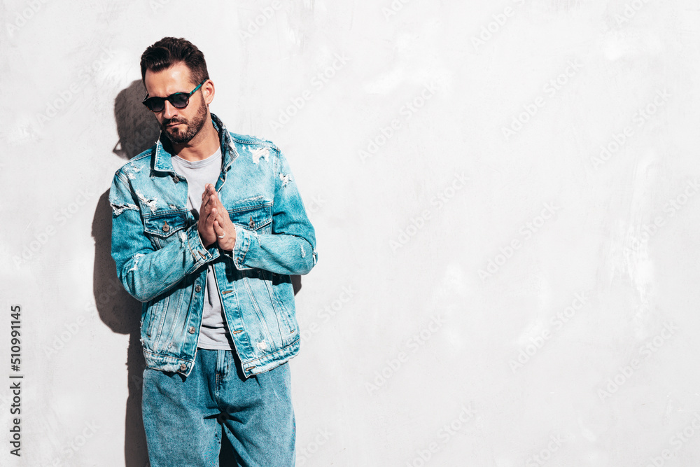 Portrait of handsome confident stylish hipster lambersexual model. Sexy man dressed in jeans jacket. Fashion male isolated on grey wall in studio. In sunglasses Portrait of handsome confident stylish hipster lambersexual model. Sexy man dressed in jeans jacket. Fashion male isolated on grey wall in studio. In sunglasses