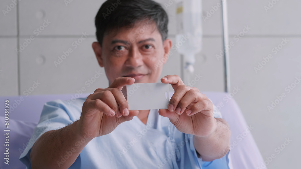 Elderly Asian male patient holding life insurance card during hospitalization. Elderly Asian male patient holding life insurance card during hospitalization.