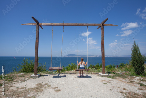 The back of the kid girl swings are playing on the sea beach © millaf