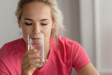 close up blonde woman drinking water after fitness workout at home