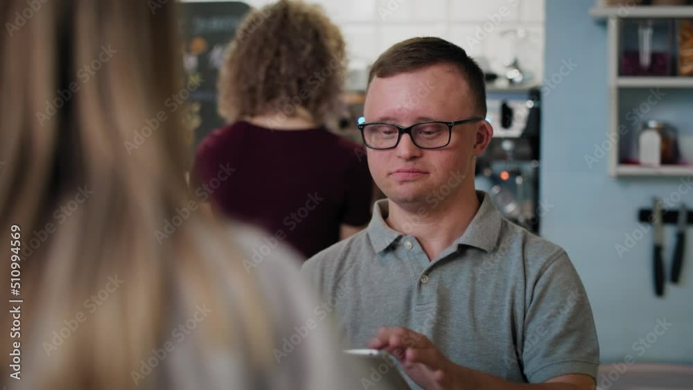 Caucasian man with down syndrome taking order in the cafe using a digital tablet. Shot with RED helium camera in 8K. Caucasian man with down syndrome taking order in the cafe using a digital tablet. Shot with RED helium camera in 8K.