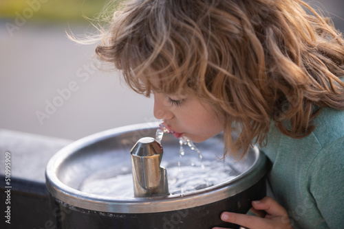 Face close up portrait of child drinking water from tap or water outdoor in park. Close up portrait of kid drinking. Thirsty child.