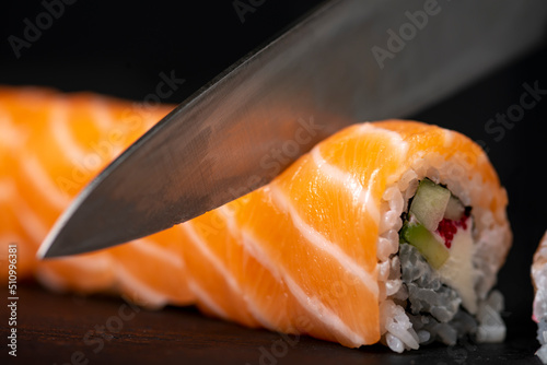 Sushi roll making at home, cutting roll with avocado and salmon, home made sushi, selective focus