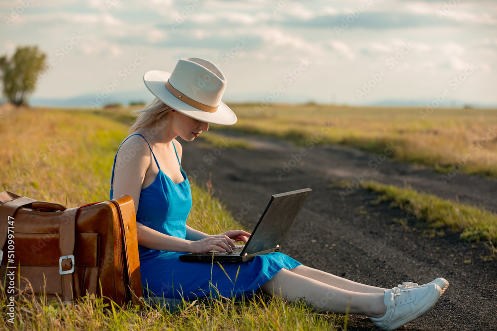 Girl in blue dress with laptop computer sit on country road in summer. Girl in blue dress with laptop computer sit on country road in summer.