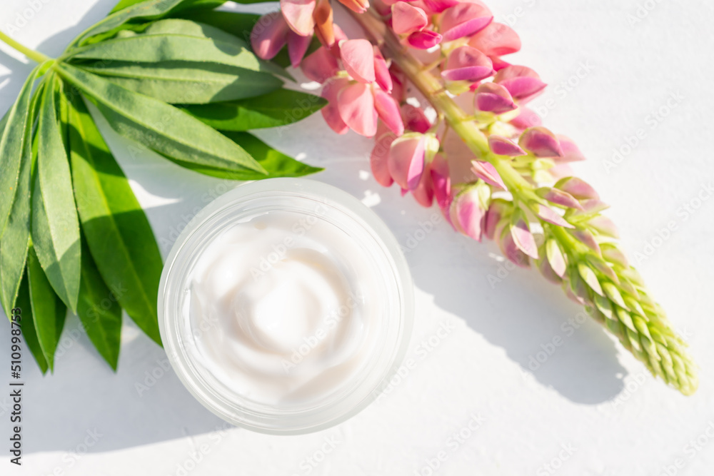 Unbranded white cosmetic cream ina open jar and bright lupine flowers on white background. Mockup, template. Container for body lotion, moisturizer cream. Unbranded white cosmetic cream ina open jar and bright lupine flowers on white background. Mockup, template. Container for body lotion, moisturizer cream.