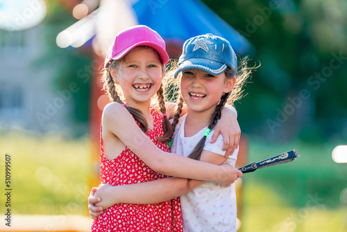 Two funny little girls of different races  in dresses and baseball caps  laughing and hugging. Best friends enjoy socializing and walking in the fresh air. Summer holidays