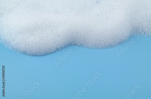 White soap or shampoo foam on blue background with copy space for text. Washing, cleaning and health care concept.