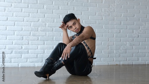 A handsome gay man sits on the floor in leather clothes and heels. LGBT community with freedom for homosexuals. An Asian model with feminine features but in a masculine body.