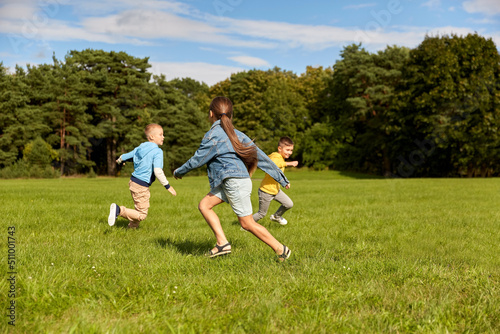 childhood, leisure and people concept - group of happy kids playing tag game and running at park