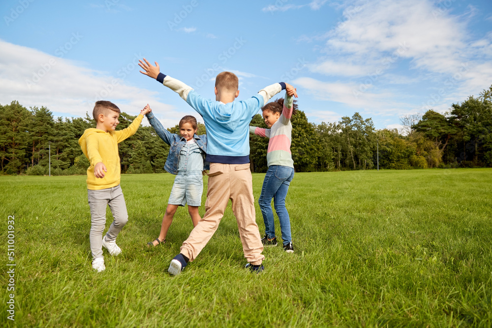 childhood, leisure and people concept - group of happy kids playing round dance at park childhood, leisure and people concept - group of happy kids playing round dance at park