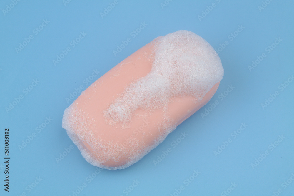 Fototapeta premium Pink soap with foam bubbles on blue background. 