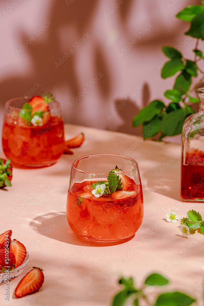 Cold summer drink - strawberry lemonade with strawberry flowers and ice cubes in glass. Summer picnic, summer sunny light, summer evening in garden. Girls party with strawberry cocktails Cold summer drink - strawberry lemonade with strawberry flowers and ice cubes in glass. Summer picnic, summer sunny light, summer evening in garden. Girls party with strawberry cocktails
