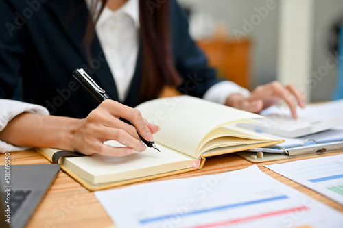 A businesswoman working at her office desk, analysing financial data and taking notes notebook.