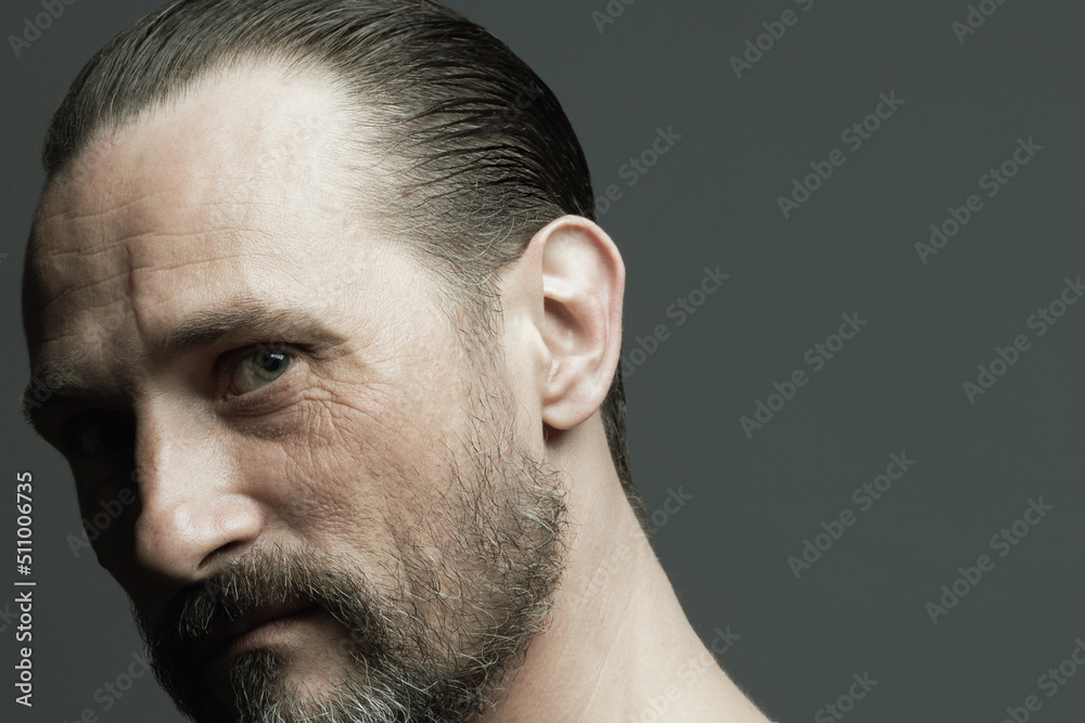 Obraz premium Male beauty concept. Fabulous at any age. Portrait of 45-year-old man standing over dark gray background. Hair brushed back. Rocker, biker style. Scar on forehead. Close up. Copy-space. Studio shot