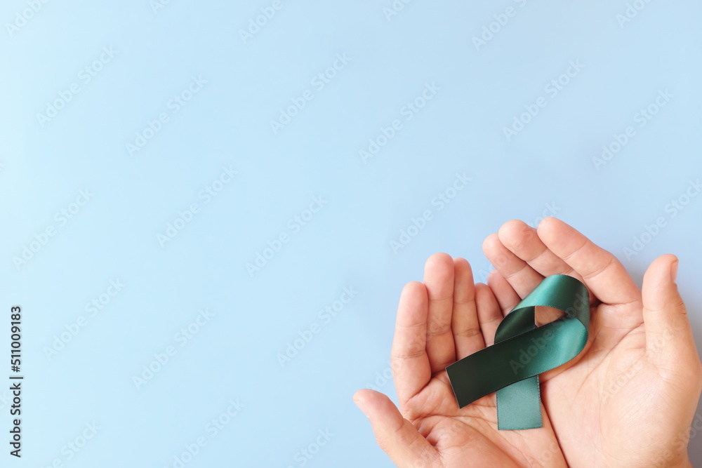 Top view of hand holding color teal awareness ribbon. PCOS, sexual assault and ovarian cancer care and prevention concept.