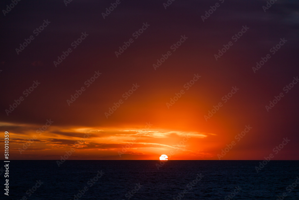 Sun with rays at sunset in the open ocean.