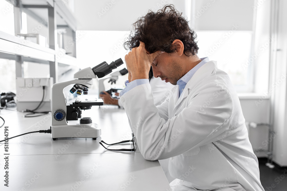 science research, work and people concept - tired male scientist with microscope working in laboratory science research, work and people concept - tired male scientist with microscope working in laboratory