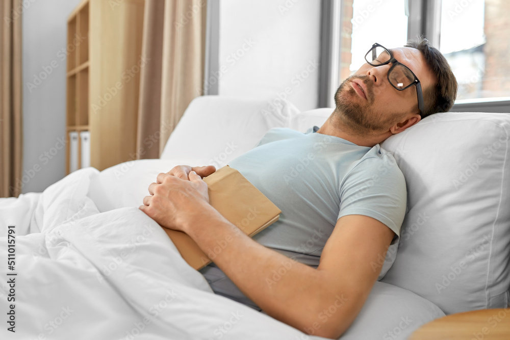 people, bedtime and rest concept - man in glasses with book sleeping in bed at home in morning people, bedtime and rest concept - man in glasses with book sleeping in bed at home in morning