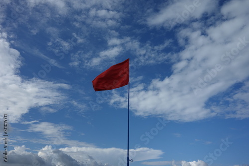 red flag on a blue cloudy sky in summer prohibit swimming