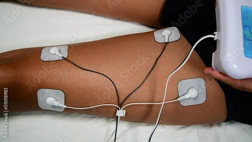 Woman using TENS (transcutaneous electrical nerve stimulation) and EMS (electronic muscle stimulation) machine at home on the muscle of one of her leg to strengthen it or pain relief