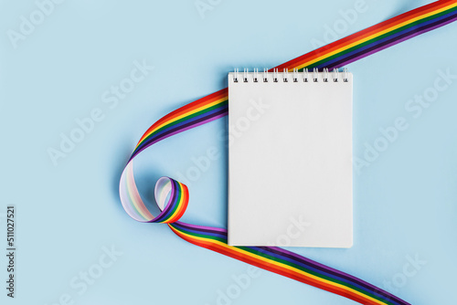 LGBT raibow flag ribbon with notebook or note mock up on light blue background. Flat lay, top view, trendy minimal composition, concept of gay pride of proud month lgbtq community. Cultural divesity photo