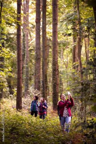 Woman Taking Photo On Mobile Phone As Group Of Female Friends On Holiday Hike Through Woods Together