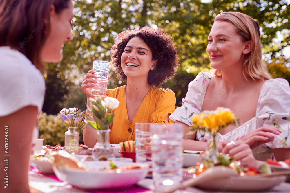 Three Female Friends Sitting Outdoors In Summer Garden At Home Eating Meal Together Three Female Friends Sitting Outdoors In Summer Garden At Home Eating Meal Together