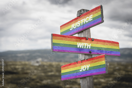 justice with joy text on wooden signpost with lgbtq flag outdoors in nature. Equality and freedom concept. © Jon Anders Wiken