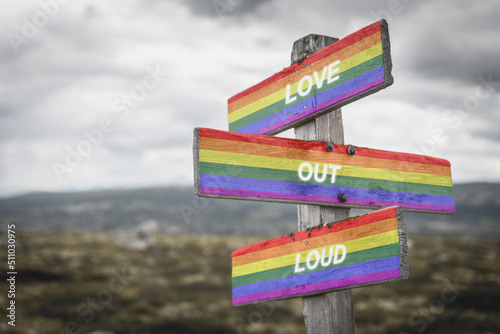 love out loud text on wooden signpost with lgbtq flag outdoors in nature. Equality and freedom concept.