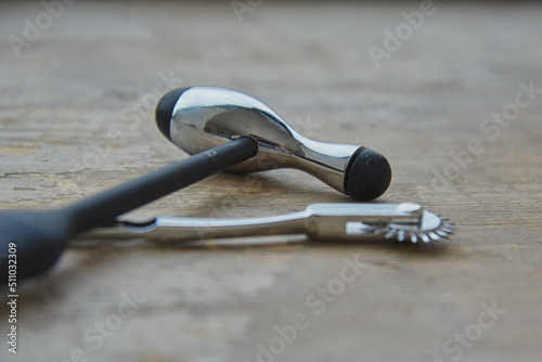 A medical reflex hammer and a Wartenberg wheel lie on a gray wooden surface.