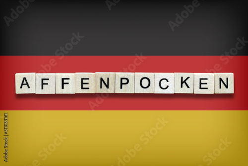 Affenpocken is the name of the monkeypox virus in German. The word is laid out with wooden cubes. On the background of the German flag. photo