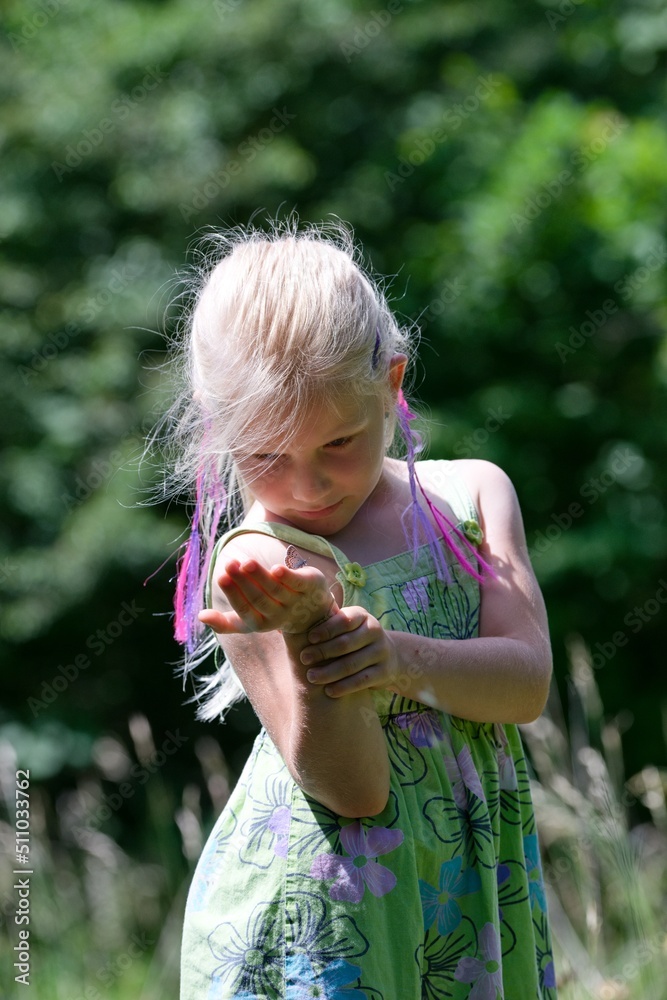 A little girl looks at a butterfly on her hand in the summer meadow A little girl looks at a butterfly on her hand in the summer meadow
