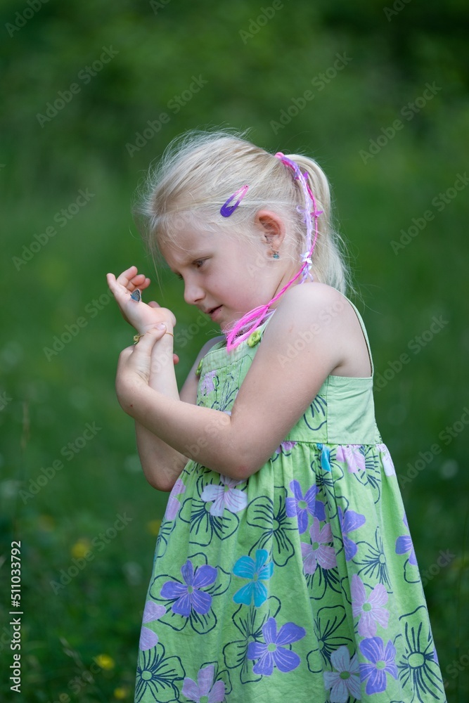 A little girl looks at a butterfly on her hand in the summer meadow A little girl looks at a butterfly on her hand in the summer meadow