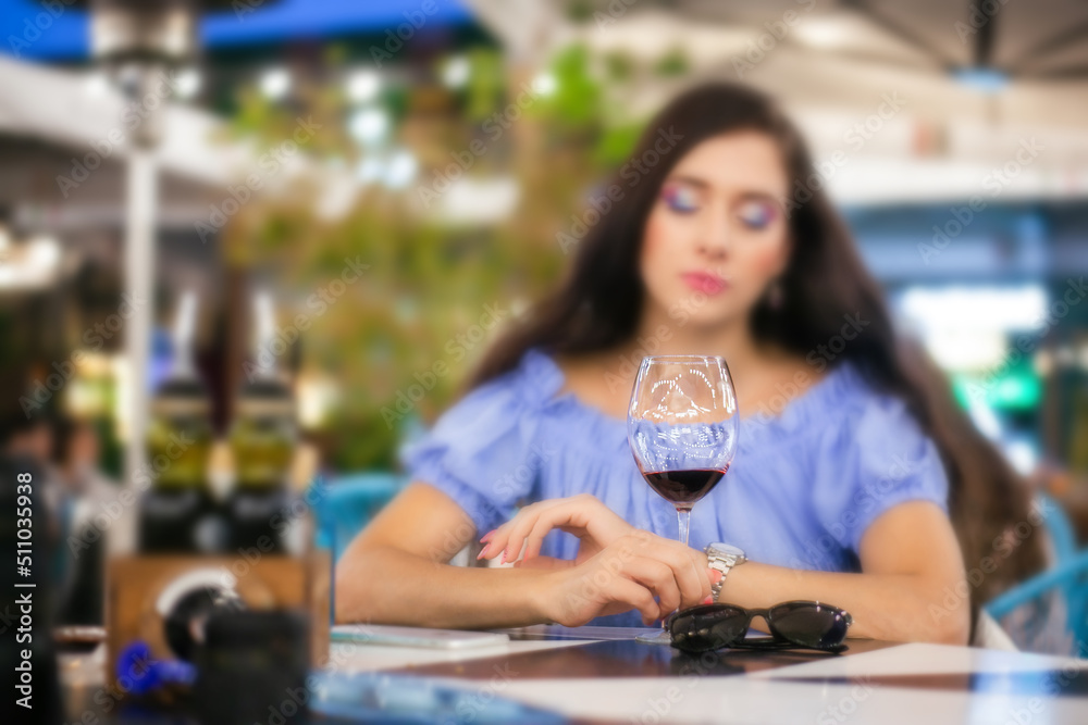 Young woman looks anxiously through a glass of wine in a street cafe, selective focus on the glass