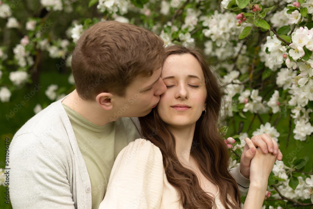 beautiful pregnant woman walks in a blooming garden. husband hugging and kisses pregnant wife beautiful pregnant woman walks in a blooming garden. husband hugging and kisses pregnant wife