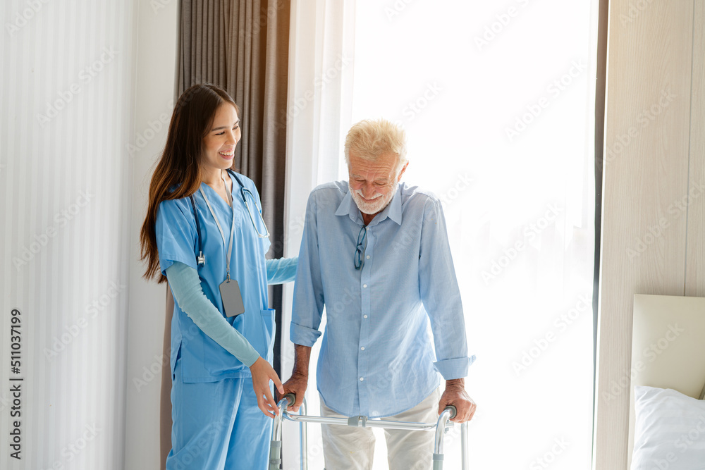 Fototapeta premium Care worker helping elderly man get out of bed and walk around the room.