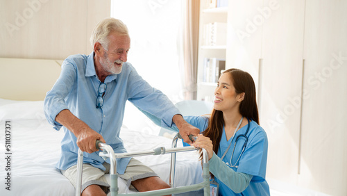 Obraz na plátně Care worker helping elderly man get out of bed and walk around the room