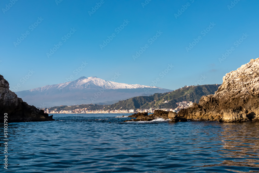 Touristic boat tour with panoramic view from open sea on snow capped volcano Mount Etna and the Ionian Mediterranean coastline near Isola Bella in Taormina, Sicily, Italy, Europe, EU. Rock formations Touristic boat tour with panoramic view from open sea on snow capped volcano Mount Etna and the Ionian Mediterranean coastline near Isola Bella in Taormina, Sicily, Italy, Europe, EU. Rock formations