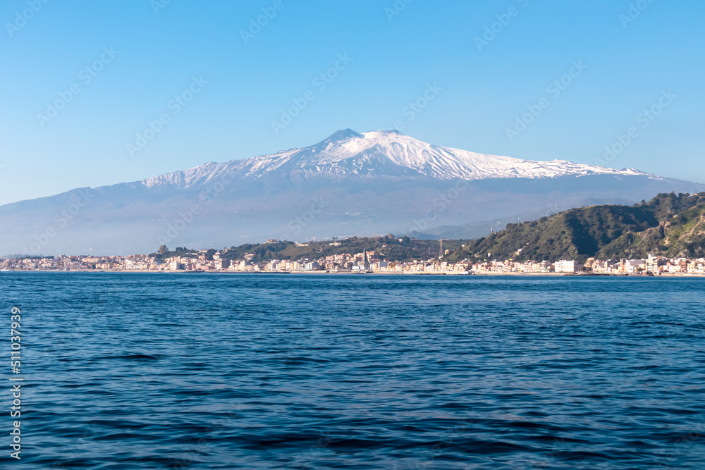 Touristic boat tour with panoramic view from open sea on snow capped volcano Mount Etna and the Ionian Mediterranean coastline near Isola Bella in Taormina, Sicily, Italy, Europe, EU. Rock formations Touristic boat tour with panoramic view from open sea on snow capped volcano Mount Etna and the Ionian Mediterranean coastline near Isola Bella in Taormina, Sicily, Italy, Europe, EU. Rock formations