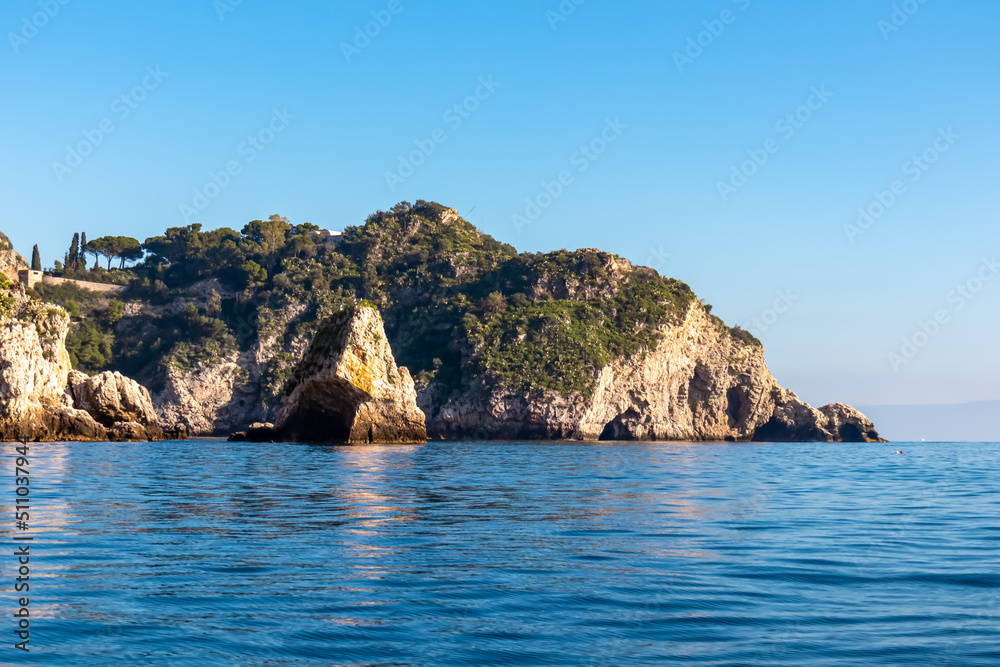 Panoramic view from the tourist island Isola Bella on the entrance of Blue Grotto (Grotta Azzurra) at Mediterranean coastline in Taormina, Sicily, Italy, Europe, EU. Calm water surface at Ionian sea