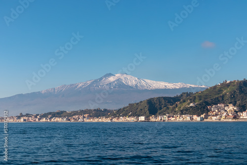 Touristic boat tour with panoramic view from open sea on snow capped volcano Mount Etna and the Ionian Mediterranean coastline near Isola Bella in Taormina, Sicily, Italy, Europe, EU. Rock formations