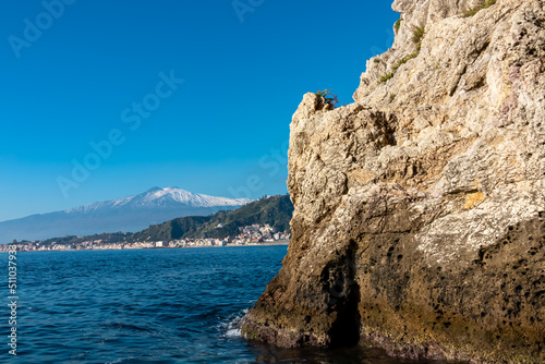 Touristic boat tour with panoramic view from open sea on snow capped volcano Mount Etna and the Ionian Mediterranean coastline near Isola Bella in Taormina, Sicily, Italy, Europe, EU. Rock formations © Chris