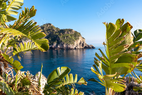Fototapeta Naklejka Na Ścianę i Meble -  Scenic view on sunny day from the touristic paradise island Isola Bella in Taormina, Sicily, Italy, Europe, EU. Tropical exotic plants in the foreground. Dreamy seascape at Ionian Mediterranean sea
