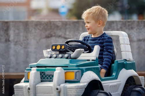 Happy blond little boy in a big toy battery powered car outdoors
