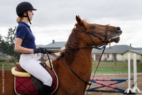 A young girl rides a brown horse, pulls on a leash to stop him