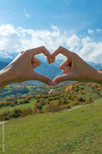 Close-up of a young woman's hands creating the shape of a love heart with her hands against the background of autumn mountains on a sunny day. Concept of travel, the passion for travel.