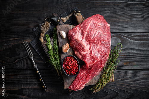Tri Tip black angus beef steak on cutting board with herbs, raw meat. Black Wooden background. Top view