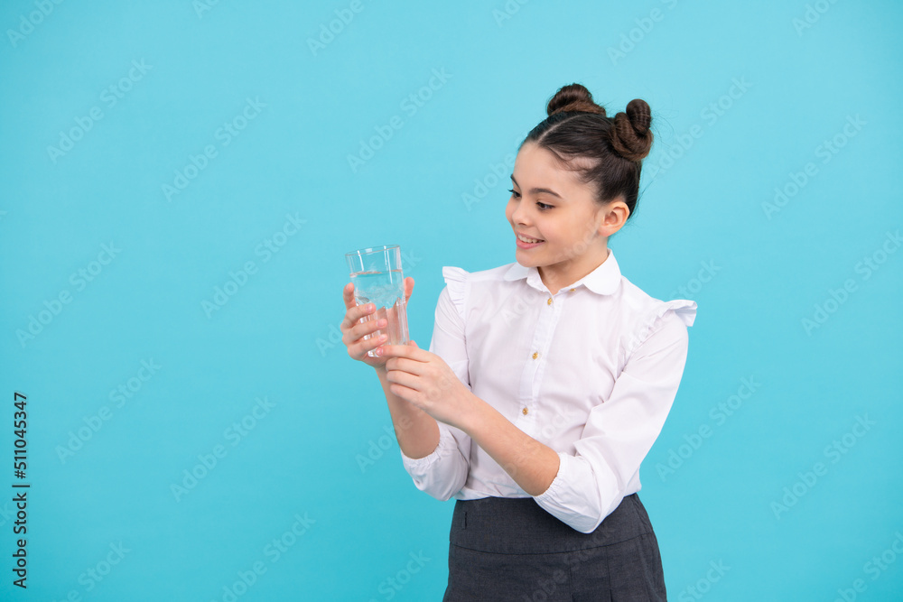 Cute teen girl drinking water from glass on blue background. Happy teenager, positive and smiling emotions of teen girl. Cute teen girl drinking water from glass on blue background. Happy teenager, positive and smiling emotions of teen girl.